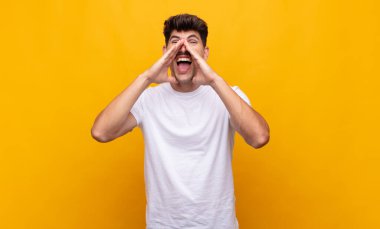 Genç yakışıklı adam mutlu, heyecanlı ve pozitif hissediyor. Elleri ağızda, bağırıyor.