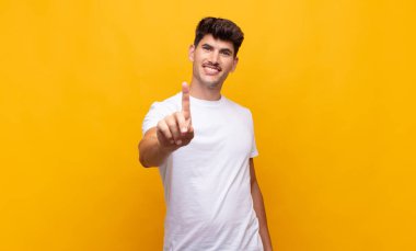 Genç ve yakışıklı bir adam gururla gülümsüyor ve gururla bir numaralı pozu veriyor, kendini lider gibi hissediyor.