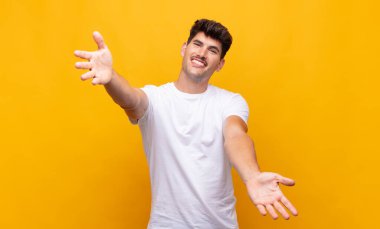 Genç yakışıklı adam neşeyle gülümsüyor sıcak, dostça, sevgi dolu bir kucak veriyor, mutlu ve sevimli hissediyor.