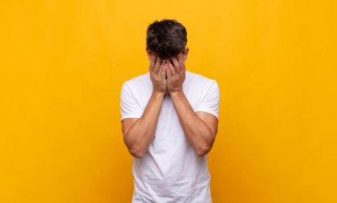 Genç yakışıklı adam üzgün, hayal kırıklığına uğramış, gergin ve depresif, iki eliyle yüzünü kaplayan, ağlayan