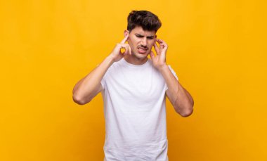 Genç yakışıklı adam sinirli, stresli ve sinirli görünüyor, iki kulağını da sağır edici bir ses, ses ya da yüksek sesle kapatıyor.