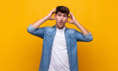 Genç yakışıklı adam heyecanlı ve şaşırmış görünüyor, ağzı açık, elleri başının üstünde, şanslı bir kazanan gibi hissediyor.