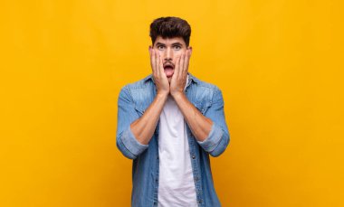 Genç yakışıklı adam şok olmuş ve korkmuş hissediyor, ağzı açık ve elleri yanaklarında korkmuş görünüyor.