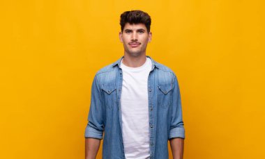 Genç yakışıklı adam pozitif ve kendinden emin gülümsüyor. Tatmin olmuş, arkadaş canlısı ve mutlu görünüyor.