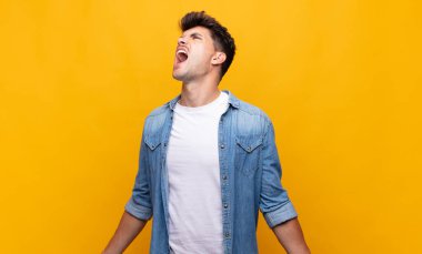 Genç yakışıklı adam öfkeyle bağırıyor, agresif bir şekilde bağırıyor, stresli ve sinirli görünüyor.