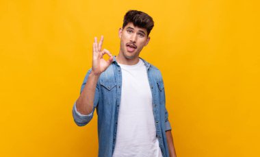 Genç yakışıklı adam kendini başarılı ve tatmin olmuş hissediyor, ağzı açık gülümsüyor, elle işaret veriyor.