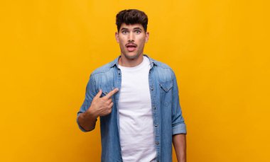 Şok olmuş ve ağzı açık, kendini işaret eden genç yakışıklı bir adam.