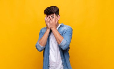 Genç ve yakışıklı bir adam korkmuş ya da utanmış hissediyor. Gözleri yarı kapalı ya da ellerle dikizliyor ya da dikizliyor.