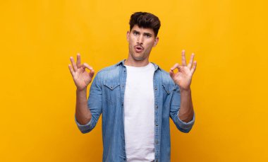 Genç yakışıklı adam şok olmuş, şaşırmış ve şaşırmış hissediyor. Onaylıyor. İki eliyle de onay işareti yapıyor.