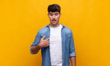 Genç yakışıklı adam neşeyle gülümsüyor, yere bakıyor ve göğsüne işaret ediyor.