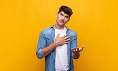 Genç yakışıklı adam mutlu ve aşık, bir eli kalbinin yanında, diğer eli önde uzanmış gülümsüyor.