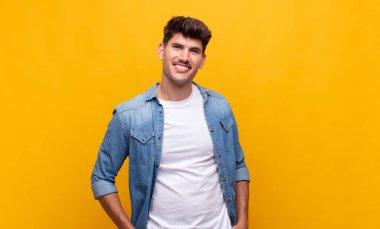 Genç ve yakışıklı bir adam neşeli, neşeli, mutlu, kendinden emin ve rahat bir ifadeyle gülümsüyor.