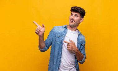 Genç, yakışıklı bir adam kendini neşeli ve şaşırmış hissediyor. Şok olmuş bir ifadeyle gülümsüyor ve bir tarafı işaret ediyor.