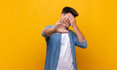 Genç ve yakışıklı bir adam elleriyle yüzünü kapatıyor ve kamerayı durdurmak için diğer elini öne koyuyor. Fotoğraf ya da resimleri reddediyor.