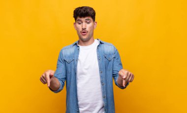 Genç yakışıklı adam şok olmuş, ağzı açık ve şaşkın, inançsızlık ve şaşkınlık içinde bakıyor ve onu işaret ediyor.