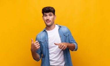 Genç yakışıklı adam neşeyle gülümsüyor ve yan taraftaki fotokopi alanını gösteriyor, mutlu ve tatmin olmuş hissediyor.