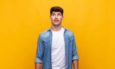 Genç yakışıklı adam şok olmuş, mutlu, şaşkın ve şaşırmış hissediyor, ağzı açık bir şekilde yana bakıyor.