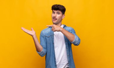 Genç yakışıklı adam neşeyle gülümsüyor ve bir objeyi göstererek veya reklamını yaparak avucundaki fotokopi alanını gösteriyor.