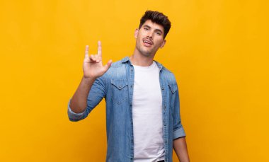 Genç yakışıklı adam kendini mutlu, eğlenceli, kendinden emin, pozitif ve asi hissediyor, elle rock ya da heavy metal işareti yapıyor.