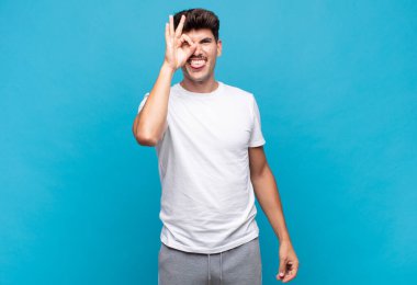 Genç yakışıklı adam mutlu bir şekilde gülümsüyor, şaka yapıyor ve gözetleme deliğinden bakıyor, sırları gözetliyor.