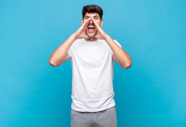 Genç yakışıklı adam mutlu, heyecanlı ve pozitif hissediyor. Elleri ağızda, bağırıyor.