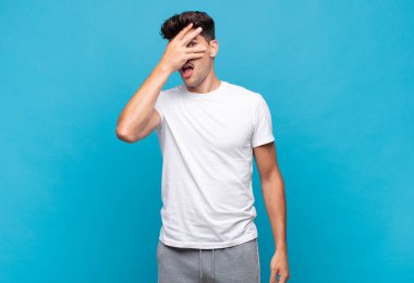 Genç yakışıklı adam şok olmuş, korkmuş ya da korkmuş görünüyor. Yüzü elle kaplanmış ve parmaklarının arasından gizlice bakıyor.