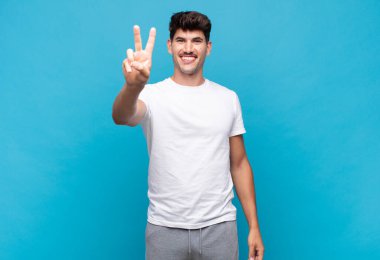 Genç yakışıklı adam gülümsüyor ve arkadaş canlısı görünüyor, iki ya da iki numarayı gösteriyor, elleri önde, geriye doğru sayıyor.