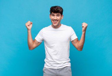 Genç yakışıklı adam çok mutlu ve şaşırmış görünüyor, başarıyı kutluyor, bağırıyor ve zıplıyor.