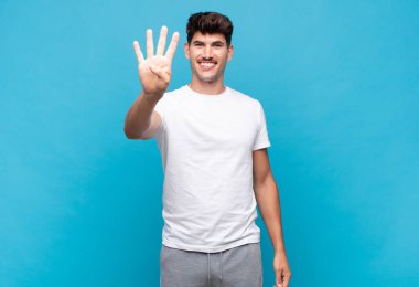 Genç yakışıklı adam gülümsüyor ve arkadaş canlısı görünüyor, 4 ya da 4 numarayı gösteriyor, eli önde, geri sayıyor.