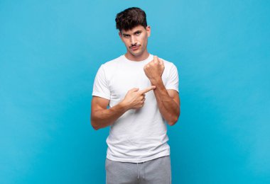 Genç yakışıklı adam sabırsız ve kızgın görünüyor, saati gösteriyor, dakiklik istiyor, zamanında gelmek istiyor.