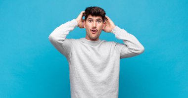 Genç yakışıklı adam heyecanlı ve şaşırmış görünüyor, ağzı açık, elleri başının üstünde, şanslı bir kazanan gibi hissediyor.