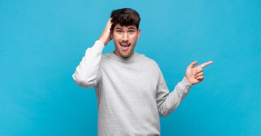 Genç yakışıklı adam gülüyor, mutlu, pozitif ve şaşırmış görünüyor. Yan fotokopi alanını işaret eden harika bir fikrin farkına varıyor.