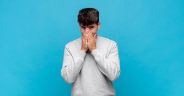 Genç yakışıklı adam mutlu ve heyecanlı, şaşırmış ve şaşırmış elleri ağızda, tatlı bir ifadeyle kıkırdıyor.