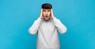 Genç ve yakışıklı bir adam hoş olmayan bir şekilde şok olmuş, korkmuş ya da endişeli görünüyor ağzı sonuna kadar açık ve iki kulağını da elleriyle kapatıyor.