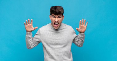 Genç ve yakışıklı bir adam panik ya da öfke içinde bağırıyor, şok olmuş, korkmuş ya da öfkeli, elleri başının yanında.