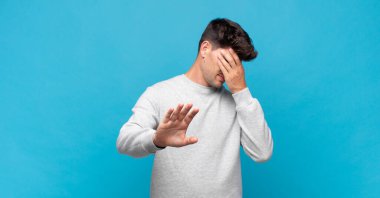 Genç ve yakışıklı bir adam elleriyle yüzünü kapatıyor ve kamerayı durdurmak için diğer elini öne koyuyor. Fotoğraf ya da resimleri reddediyor.