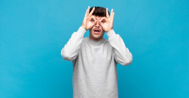 Genç yakışıklı adam şaşkın, şaşırmış ve şaşırmış hissediyor. Elinde şaşkın, inançsız bir bakışla gözlük tutuyor.