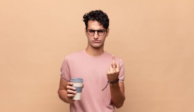 Genç ve yakışıklı bir adam kahveyle kızgın, sinirli, isyankar ve agresif, orta parmağını sallıyor, karşı koyuyor.