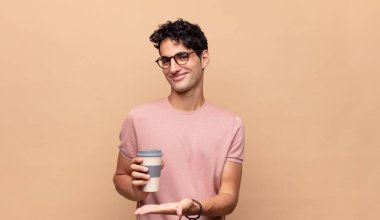 Kahveli genç ve yakışıklı bir adam neşeli bir şekilde gülümsüyor, mutlu hissediyor ve fotokopi alanında avuç içi dolu bir konsept gösteriyor