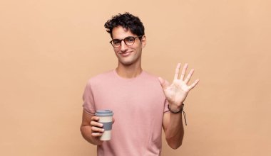 Kahveli genç yakışıklı adam gülümsüyor ve arkadaş canlısı görünüyor, 5 ya da 5 numarayı gösteriyor, eli önde, geri sayıyor.