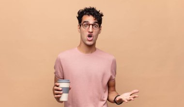Genç ve yakışıklı bir adam kahveyle şoke olmuş, şaşırmış, endişeli ve paniklemiş, stresli ve dehşete kapılmış bir şekilde bakıyor.