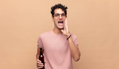 Birası olan genç bir adam mutlu, heyecanlı ve pozitif hissediyor, elleri ağızının yanında bağırıyor, bağırıyor