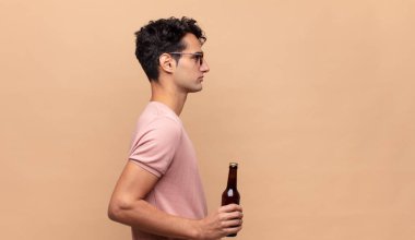 Profil görünümünde birası olan genç adam ilerideki boşluğu kopyalamaya çalışıyor, düşünüyor, hayal ediyor ya da hayal kuruyor.