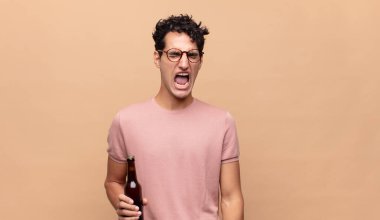 Elinde bira olan genç adam agresif bir şekilde bağırıyor, çok kızgın, sinirli, öfkeli ya da sinirli görünüyor, haykırmıyor