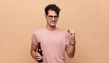 Elinde bira olan genç adam sinirli bir ifadeyle agresif bir şekilde bağırıyor ya da yumruklarıyla başarıyı kutluyor.