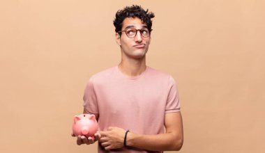 Kumbaralı genç adam omuz silkiyor, kafası karışık ve kararsız, kolları bağlı ve şaşkın görünüyor.