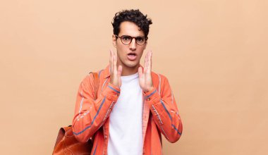 Genç öğrenci şok olmuş ve korkmuş hissediyor, ağzı açık ve elleri yanaklarında korkmuş görünüyor.