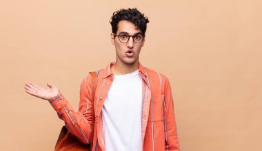 Genç öğrenci şaşırmış ve şoka uğramış görünüyor, çenesi düşmüş ve eli açık bir nesneyi tutuyor.