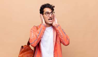 Genç öğrenci kendini mutlu, heyecanlı ve şaşırmış hissediyor, iki eli yüzü üzerinde yana bakıyor.