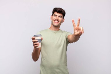 Kahveli genç adam gülümsüyor ve mutlu görünüyor, kaygısız ve pozitif, zafer ya da barışı simgeliyor.